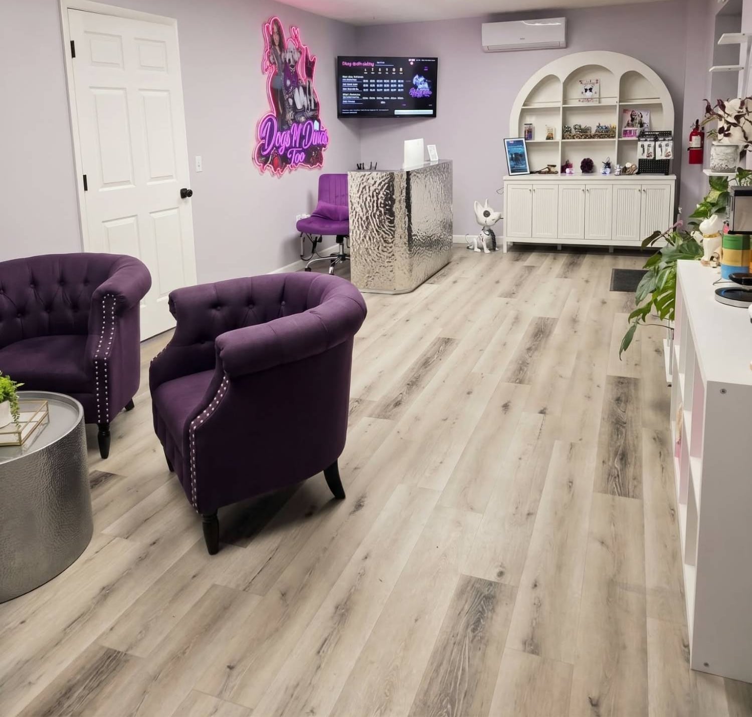 Dogs N Divas Too salon lobby with purple tufted chairs, neon sign and arched white display shelves